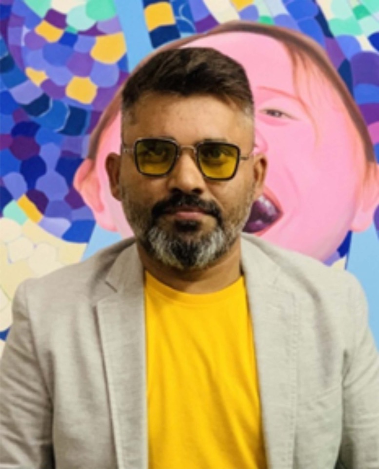 Sambit Kumar Panda in yellow-tinted glasses, in front of one of his own paintings.