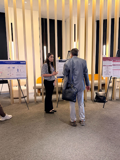 Ariya Mukherjee-Gandhi presenting the poster at the conference, standing beside it on an easel.